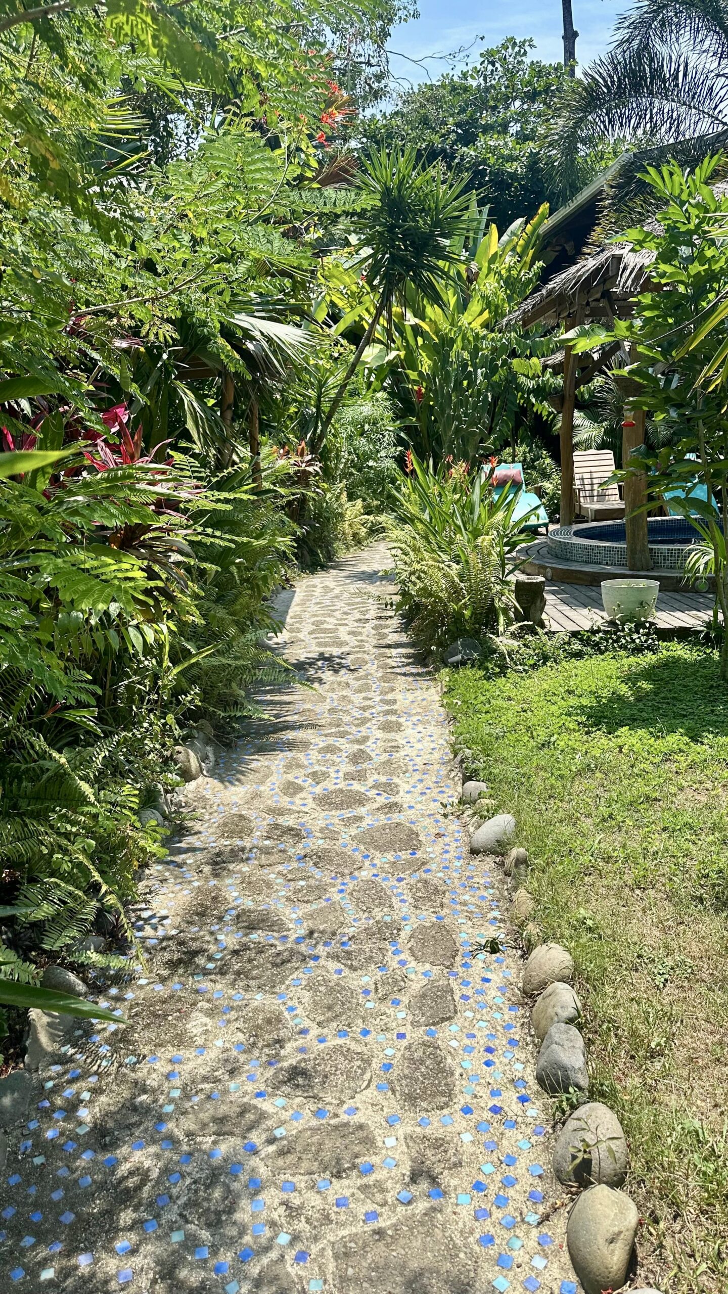 Stone path with blue mosaic details winding through vibrant tropical gardens at Casa Mambo.