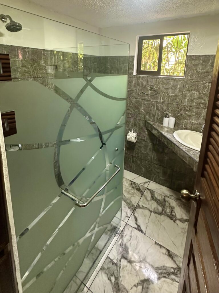 Modern bathroom with frosted glass shower, marble floors, and garden view window in Room 1 at Casa Mambo